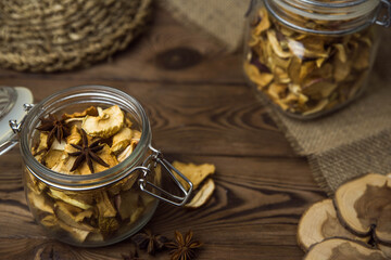 Homemade crispy sun dried organic apple slices. Close up of apple chips with spice in glass jar on brown wooden background with copy space for text
