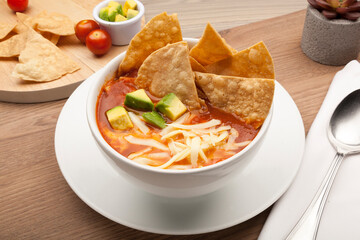Mexican soup with tortilla chips, avocado and cheese in a white bowl on a rustic wooden table