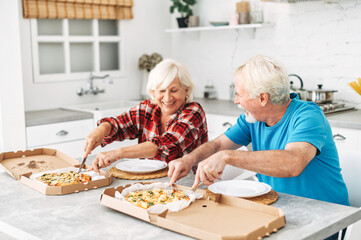 Senior couple eating pizza in the kitchen