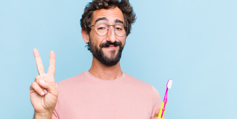 young bearded man looking happy, confident and trustworthy, smiling and showing victory sign, with...