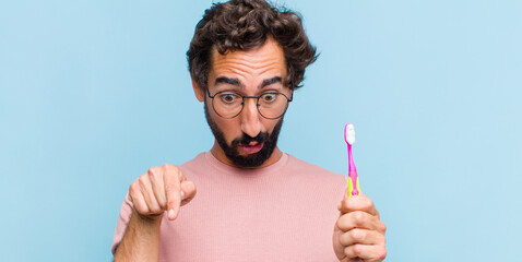young bearded man feeling shocked, open-mouthed and amazed, looking and pointing downwards in...
