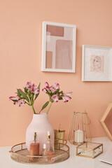 Two pictures in frames on wall by table with flowers in vase and other stuff