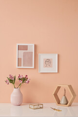 Two pictures in frames on pink wall by table with flowers in white ceramic vases