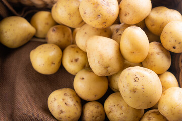 New raw potatoes in a wicker basket on a brown background close up