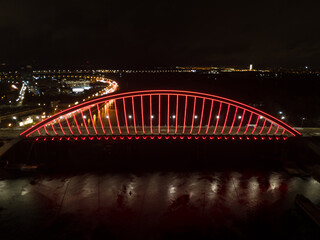 Obraz premium Aerial drone view. Modern arch cable-stayed bridge in Kiev in the evening. Colored lighting of the arch of the bridge.