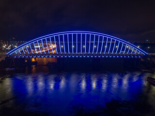 Obraz na płótnie Canvas Aerial drone view. Modern arch cable-stayed bridge in Kiev in the evening. Colored lighting of the arch of the bridge.
