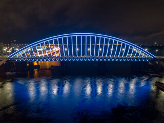 Aerial drone view. Modern arch cable-stayed bridge in Kiev in the evening. Colored lighting of the arch of the bridge.
