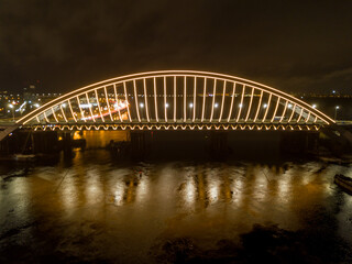 Aerial drone view. Modern arch cable-stayed bridge in Kiev in the evening. Colored lighting of the arch of the bridge.