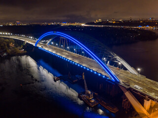 Aerial drone view. Modern arch cable-stayed bridge in Kiev in the evening. Colored lighting of the arch of the bridge.