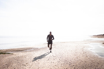 Black sportsman who practices running on the beach with a back light. Concept of health and sport.
