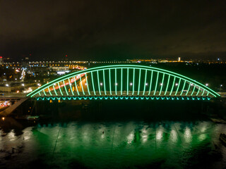 Aerial drone view. Modern arch cable-stayed bridge in Kiev in the evening. Colored lighting of the arch of the bridge.