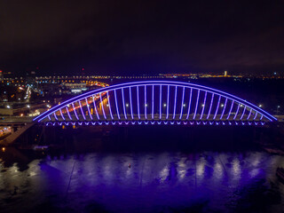 Fototapeta na wymiar Aerial drone view. Modern arch cable-stayed bridge in Kiev in the evening. Colored lighting of the arch of the bridge.