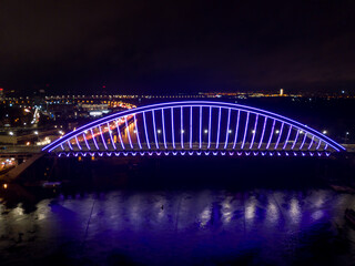 Fototapeta na wymiar Aerial drone view. Modern arch cable-stayed bridge in Kiev in the evening. Colored lighting of the arch of the bridge.
