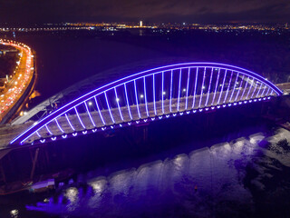 Obraz premium Aerial drone view. Modern arch cable-stayed bridge in Kiev in the evening. Colored lighting of the arch of the bridge.