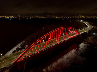 Aerial drone view. Modern arch cable-stayed bridge in Kiev in the evening. Colored lighting of the arch of the bridge.