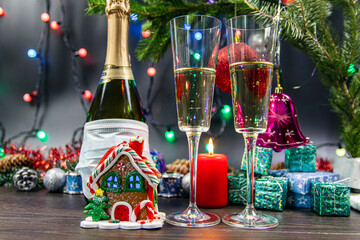 Two glasses of champagne with gas bubbles. Christmas gingerbread in the form of a colorful house. Christmas decoration with a red burning candle.