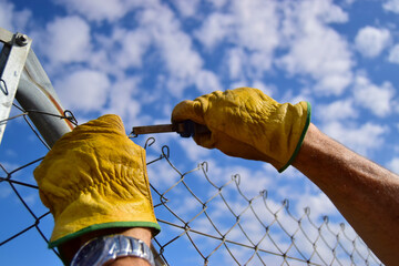 Manos de hombre con guantes trabajando con alicates y alambre. Restauración del cercado.