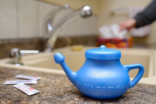 Man at the sink reaching for tissues with blue Neti Pot for nasal irrigation on the kitchen counter Toronto, Canada - March 28, 2014