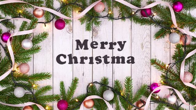 Merry Christmas text appear in frame with pine branches pink ornaments and blinking lights. Stop motion