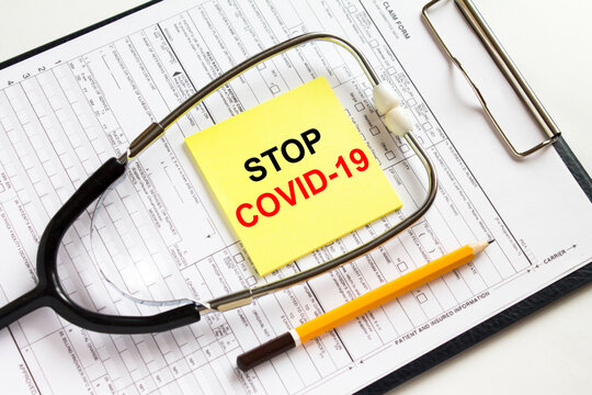 Text Stop Covid-19 on a yellow sticker with a stethoscope lying on a folder with medical documents