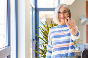 middle age woman smiling and looking friendly, showing number four or fourth with hand forward,...
