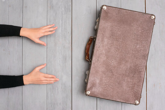 Female hands and old retro suitcase on the wooden floor background. Top view.