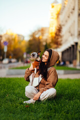 Fototapeta na wymiar Happy woman sitting on a green lawn with a dog breed biewer terrier in her arms, looking at a pet with a smile on his face. Smiling lady spends time with a dog.