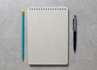 A spring notebook with a sheet of craft paper A5 with a ballpoint pen and simple green graphite pencil on light grey concrete background. Concept of new idea, business plan and strategy.