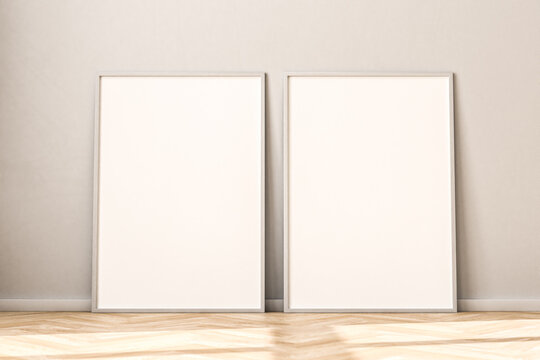 Two empty Picture Frames on parquet floor leaning against bright wall. Sunlight flooding in from the left. 3d render mockup.