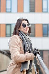 woman in sun glasses and coat standing on the bridge in atumn city