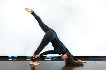 A strong and flexible woman is seen in a one legged dog posture during an advanced Vinyasa flow yoga session, with copy space on both sides.