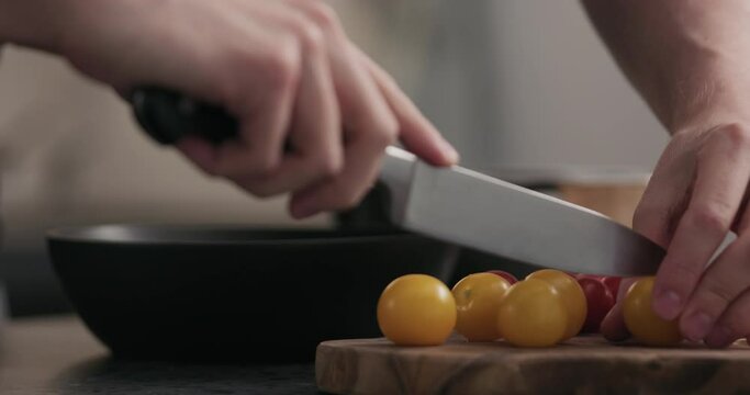 Slow motion man cuttting cherry tomatoes in halves on olive wood board
