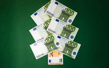 Banking and Finance. Christmas tree made of European currency banknotes in green and orange colors on a bright green background. Cash in the form of a Christmas tree. Banking and Finance.