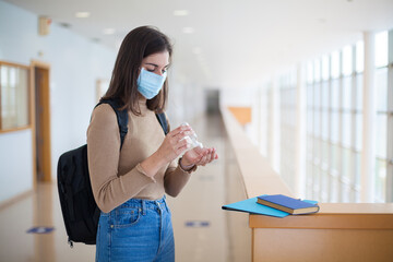 Fototapeta na wymiar Female university student wearing mask and using hand sanitizer gel during covid-19