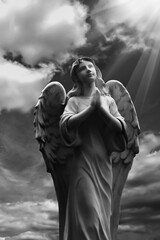 Human soul as angel with wings looking up at the sky in rays of light. Ancient statue. Black and white image.