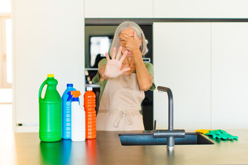 middle age woman covering face with hand and putting other hand up front to stop camera, refusing...