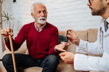 Obraz premium Young handsome doctor visiting examining his senior male patient at his home.