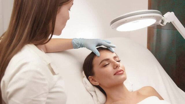 cosmetologist cheking female skin on face at beauty clinic