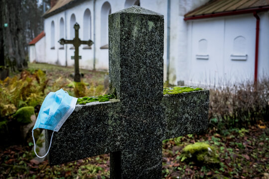 Victim Of Coronavirus Covid 19, Conceptual Photo With Protective Medical Mask On A Stone Tomb In The Cemetery. Death From Covid 19