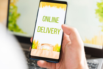 Hand with mobile phone. Online internet shopping, order through mobile application. Laptop. Home delivery of food, groceries from grocery store. Paper bag with pasta on screen. Payment by credit card