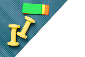 Yellow dumbbells and a set of multi-colored elastic bands for fitness on a sports mat and a white background diagonally.