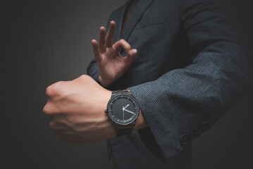 Business man is showing his wrist watch close up and gesturing the ok sign by his hand. Work done on time.