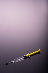 Yellow Syringe on glossy black background.  Dark side of Immunization, vaccination, or drugs and darkness conmcept.