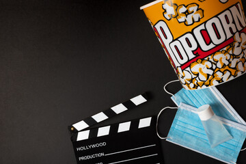 Movie clapperboard, hydrogel, face mask, and popcorn box on a black background during the second wave of the coronavirus pandemic. Covid concept.