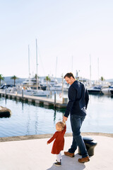Man is walking hand in hand with his sweet 2-year old on a boat pier