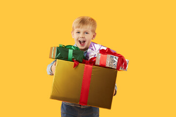 Portrait of happy cute child boy holding gift boxes and looking at camera isolated on yellow background