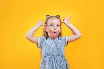 Child girl making a face and showing her tongue on yellow background - obrazy, fototapety, plakaty