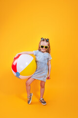 Funny happy child in sunglasses holding beachball on yellow background