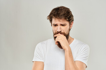 A man in a white t-shirt with a beard emotions displeased facial expression light background