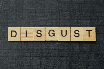 gray word disgust from small wooden letters on a black table
